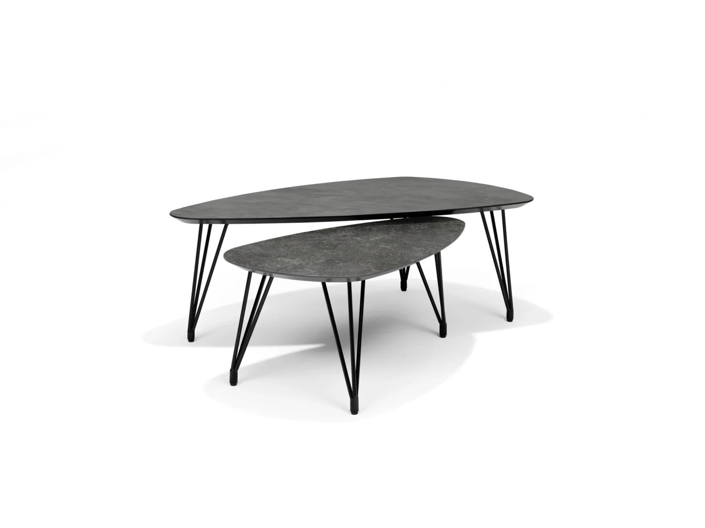 De Salontafel Grijs 130 x 70 CM MDF bestaat uit twee moderne salontafels met onregelmatige donkergrijze bladen en zwarte metalen haarspeldpoten op een witte achtergrond. De kleinere tafel schuift gedeeltelijk onder de grotere.