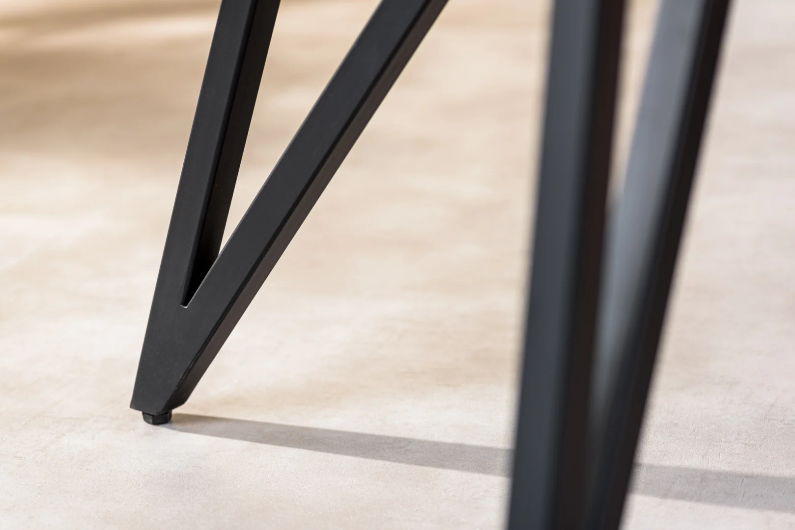 Close-up van de moderne zwart metalen poten van de Eettafel, 240x110 cm, B340 zwart, op een lichtbeige vloer met subtiele schaduwen.