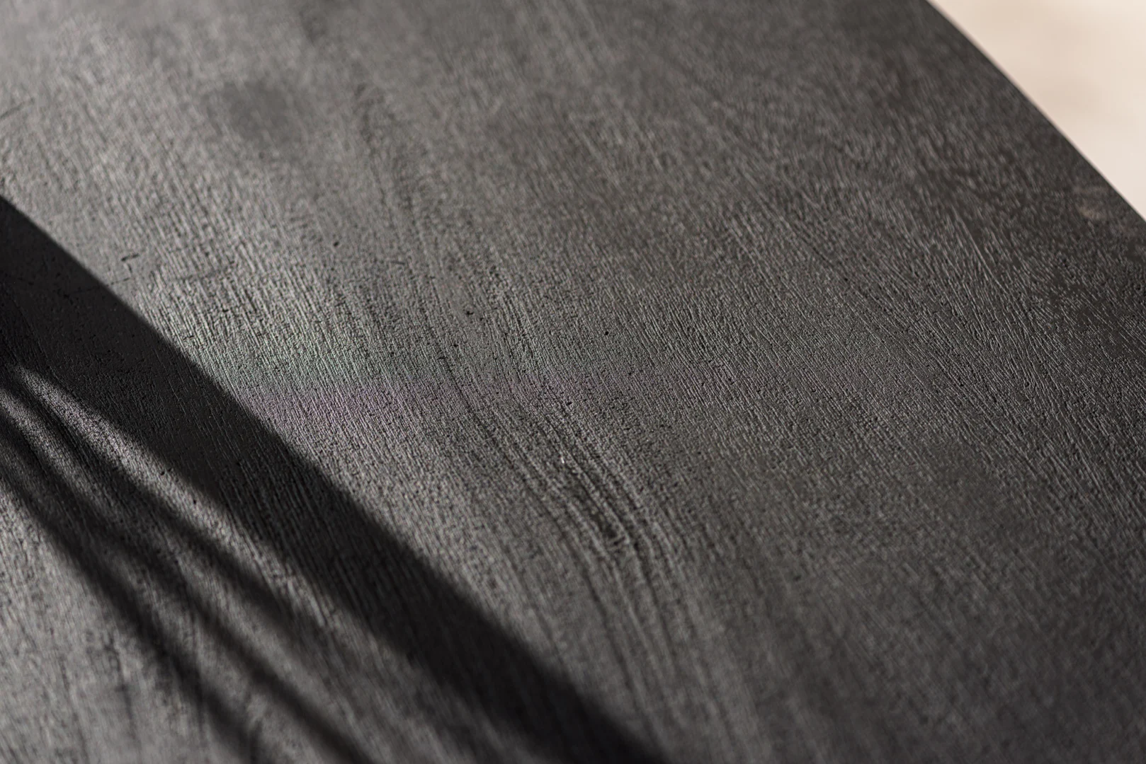 Close-up van de Eettafel (240x110 cm, B340 zwart) met het donkere, getextureerde houten oppervlak en diagonale lijnen van licht en schaduw linksboven.
