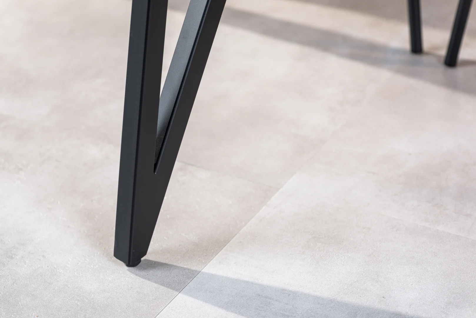 Close-up van de zwarte metalen poot van de Eettafel, 240x110 cm, B340 zwart, op een lichtgekleurde tegelvloer met de schaduw zichtbaar op de tegels.