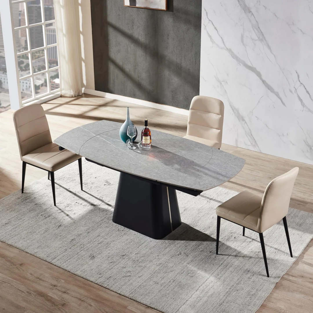 In een moderne eetkamer staat de Rick Uitschuiftafel 160x90 (+2 x 40cm) Deckstone Zwart Marmer op een licht vloerkleed, omringd door drie beige stoelen. Twee vazen en een fles staan op tafel terwijl het zonlicht door de grote ramen naar binnen schijnt.