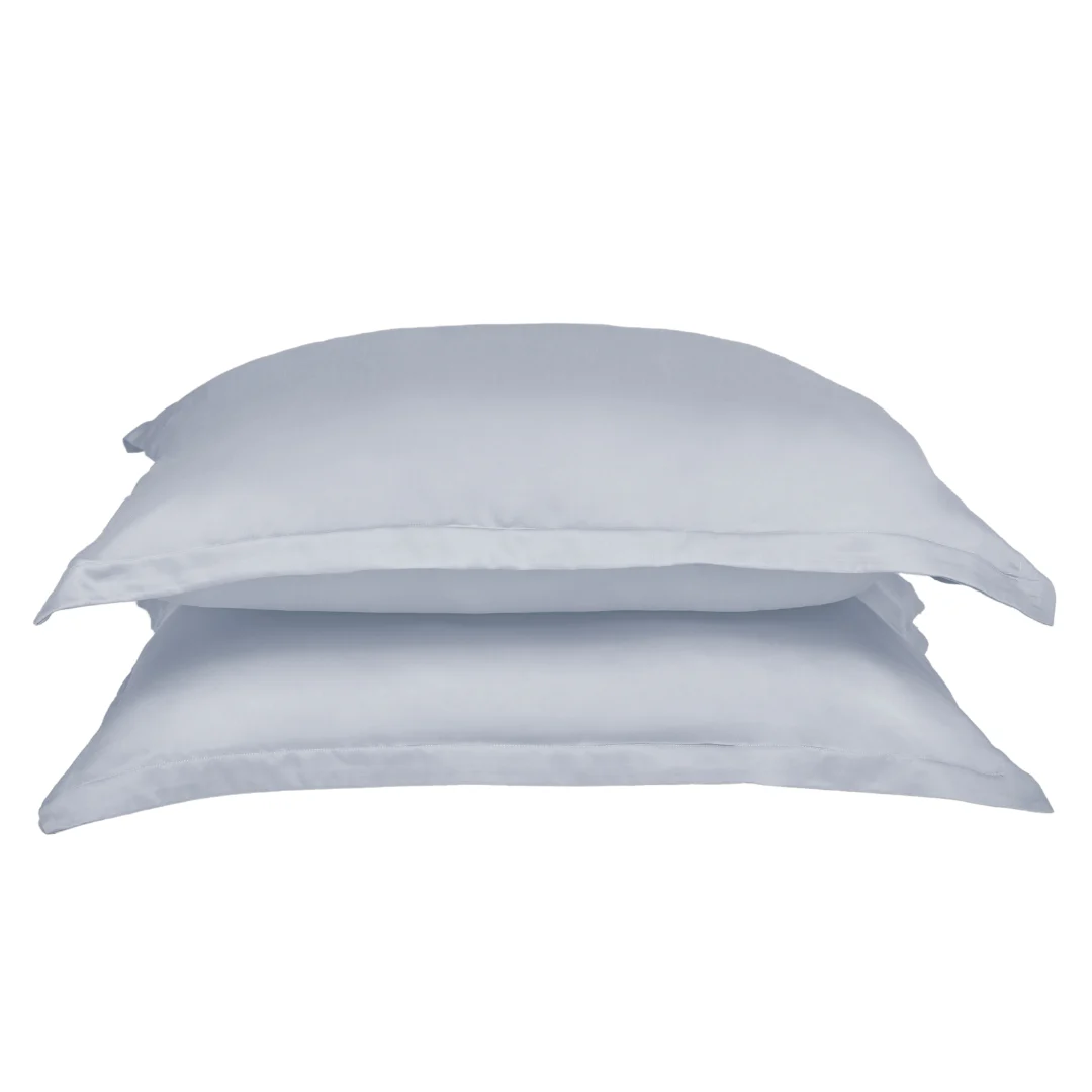 Twee gestapelde, lichtblauwe kussenslopen van Tencel, zonder volant, op een witte achtergrond. Zachte belichting benadrukt de gladde textuur.