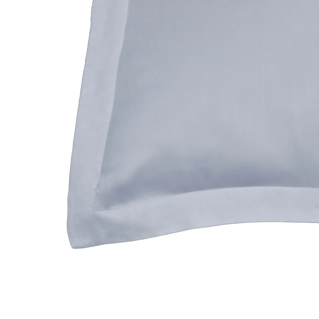 Detailopname van een lichtblauwe kussensloop, gemaakt van zachte stof. Het kussen heeft een strakke rand en is gefotografeerd tegen een witte achtergrond.