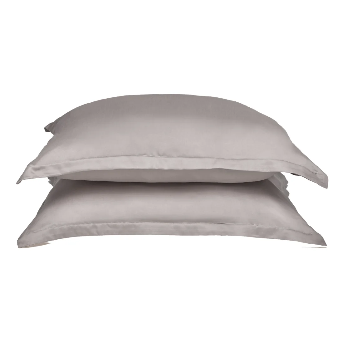 Gestapelde, zachtgrijze kussenslopen van TENCEL Lyocell op een witte achtergrond. De stof heeft een subtiele glans en zachte belichting.