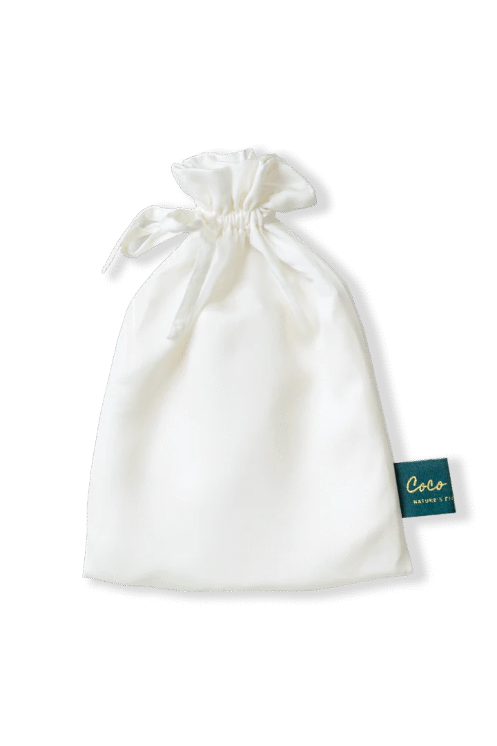 Witte satijnzachte kussensloop verpakt in een zakje met trekkoord. Zachte belichting en een label met de tekst Coco Nature's Fit.