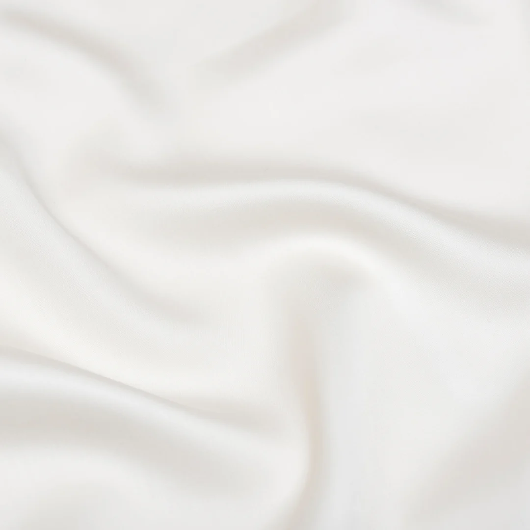 Close-up van een witte, satijnzachte kussensloop met subtiele plooien. Zachte belichting benadrukt de gladde textuur van de Tencel™ stof.