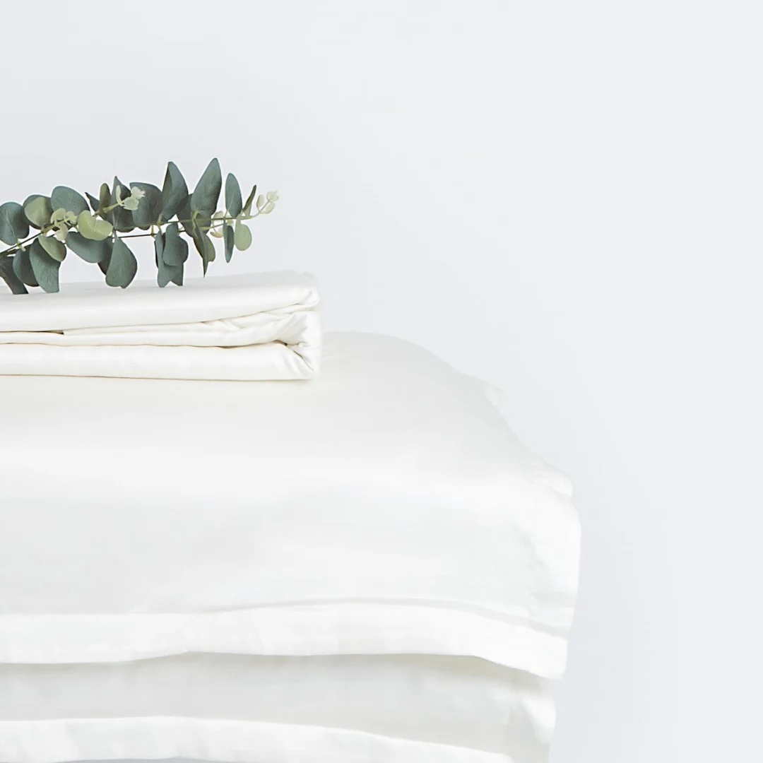 Een netjes gevouwen Dekbedovertrek 200x220 Makkelijk combineren in wit, met een enkele eucalyptusstengel erop, tegen een effen witte achtergrond.