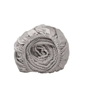 Gegroefd, opgerold grijs hoeslaken van Tencel, close-up. Zachte textuur, subtiele schaduwen. Witte achtergrond. Studiofotografie.