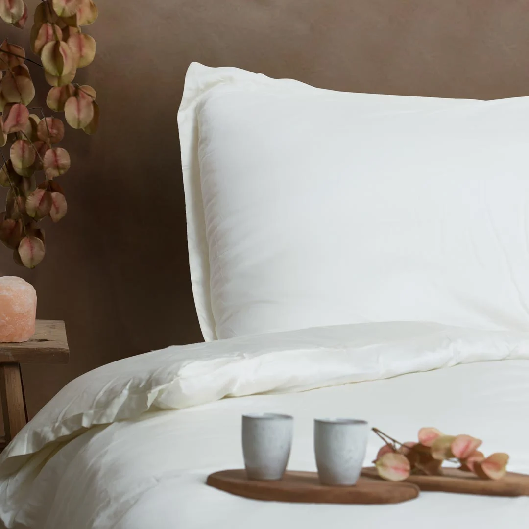 Op een netjes opgemaakt bed ligt Dekbedovertrek 200x220 Topkwaliteit textiel in wit, met bijpassende kussens. Op een houten dienblad staan twee kopjes en gedroogde bladeren. Naast het bed staat een bijzettafeltje met een roze zoutlamp en een vaas met gedroogde bladeren tegen een bruine muur.