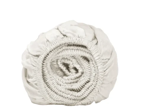 Oprol van wit hoeslaken, close-up. Elastische randen zichtbaar. Zachte belichting, effen witte achtergrond. Tencel Lyocell materiaal.