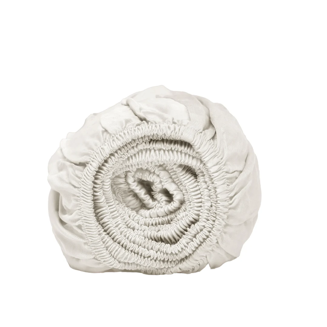 Oprol van wit hoeslaken, close-up. Elastische randen zichtbaar. Zachte belichting, effen witte achtergrond. Tencel Lyocell materiaal.