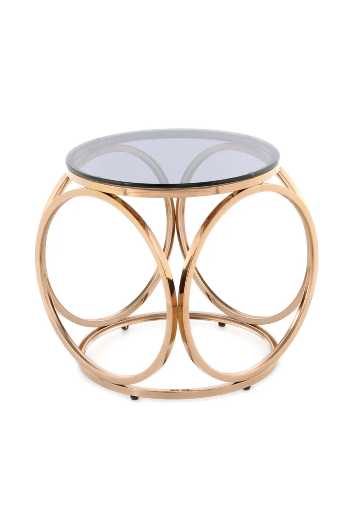De Bijzettafel Grijs Staal Chique is een ronde bijzettafel met een blad van gerookt glas en een cirkelvormig frame van metallic goud met kruisende ringvormige steunen.