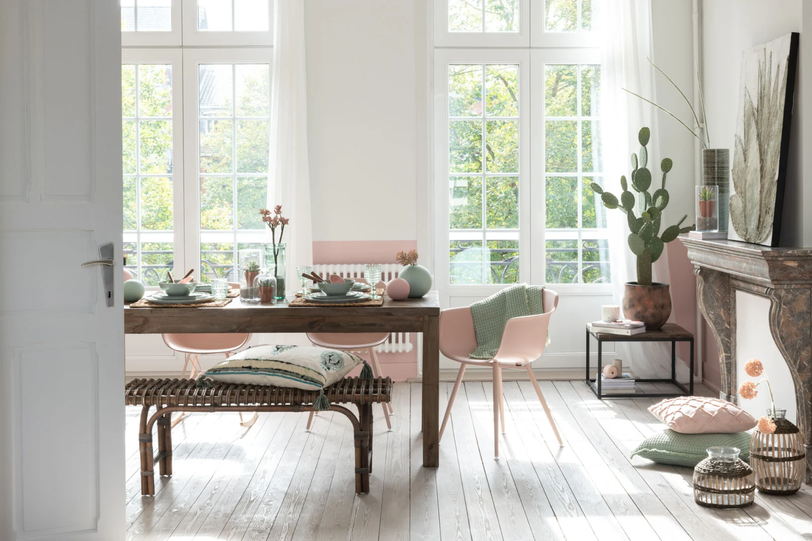 Lichte eetkamer in zacht licht met de Bijzettafel Zwart, Bruin 60 x 41 CM vierkant metaal tafel, gecombineerd met roze stoelen, een bank met kussens, groen en roze decor, weelderige planten en een rustieke open haard.