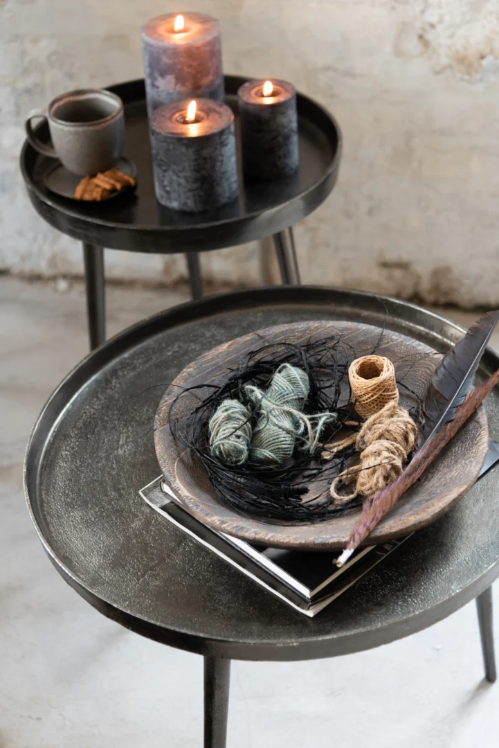 Twee Bijzettafel Donkergrijs, Greige 61 x 61 CM ronde aluminium tafels tonen brandende kaarsen, een koffiekopje, een koekje en een houten schaal met garen, veren en notitieboekjes en creëren zo een gezellige, neutrale, rustieke sfeer.