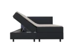 Zijaanzicht van een donkerblauwe boxspring met opbergruimte. Het bed is gedeeltelijk open, waardoor de opbergruimte zichtbaar is.