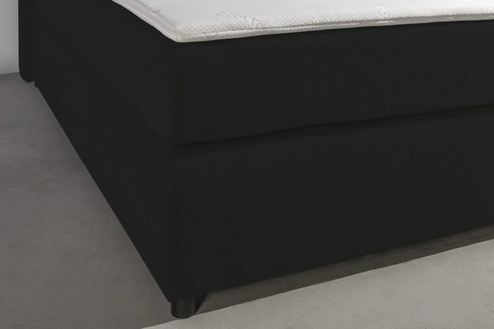 Detailopname van een zwarte boxspring met topper, laag standpunt. Zachte belichting, minimalistische stijl.