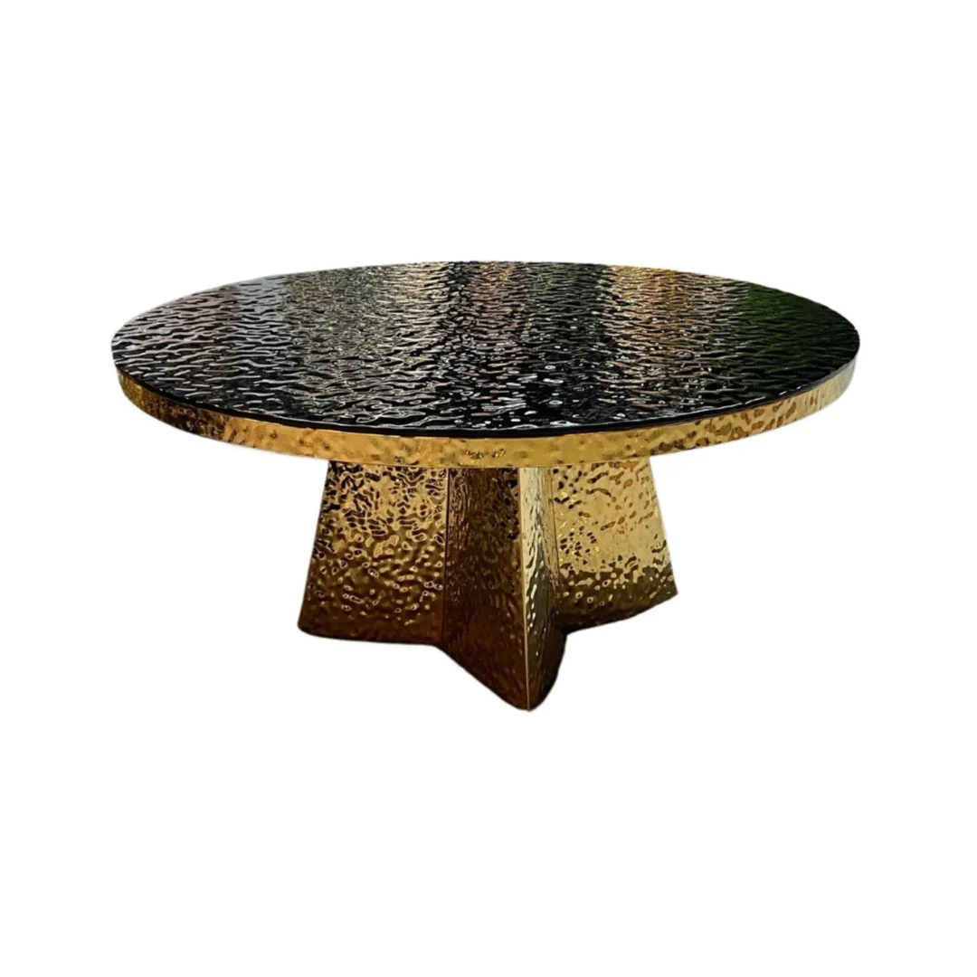 De Eettafel JIMMY 110 x 110 CM is een robuuste ronde tafel met een modern, luxe zwart gestructureerd glazen blad en een breed goudkleurig, gehamerd metalen onderstel voor stevige ondersteuning.