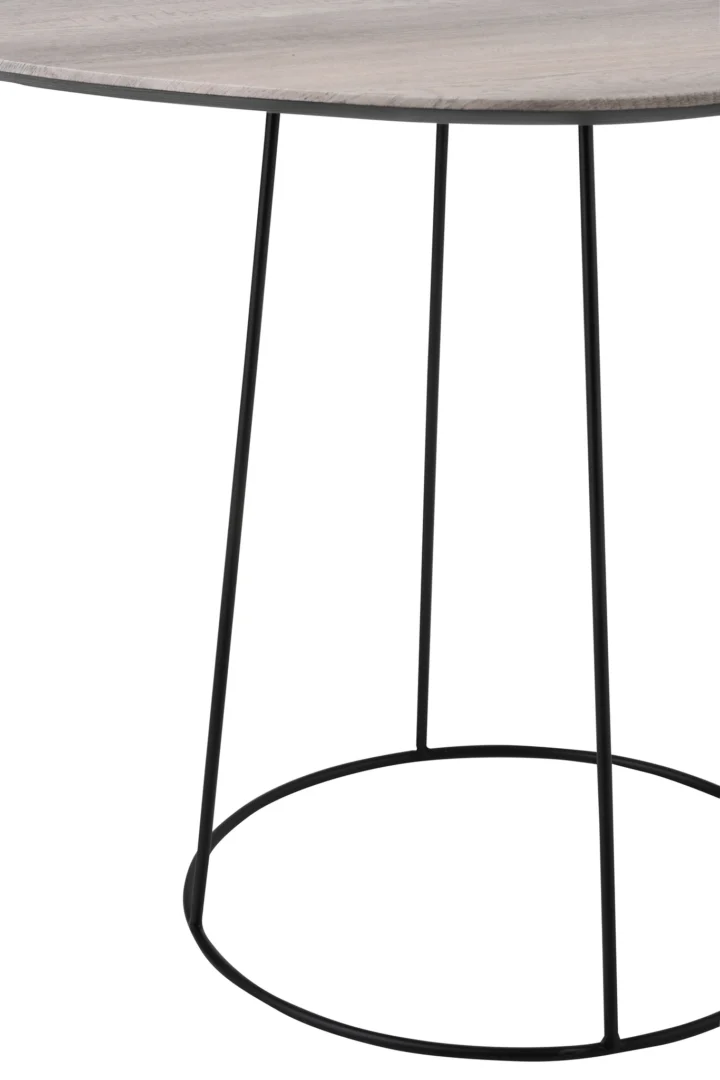 Een close-up van de Bijzettafel Greige, Zwart 55 CM Ovaal laat het licht houtlook ovale blad en de slanke zwarte ijzeren poten zien, aan de basis verbonden door een ronde ijzeren steun.