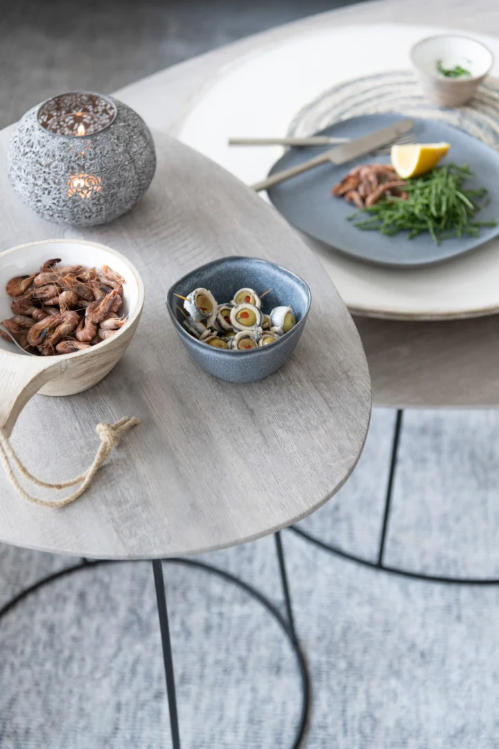 De Bijzettafel Greige, Zwart 55 CM Ovaal (ijzer) bevat schaaltjes met gedroogde garnalen, gemarineerde olijven, groentjes, citroen en gekookt vlees. Een stijlvolle kandelaar op tafel creëert een gezellige eetsfeer.