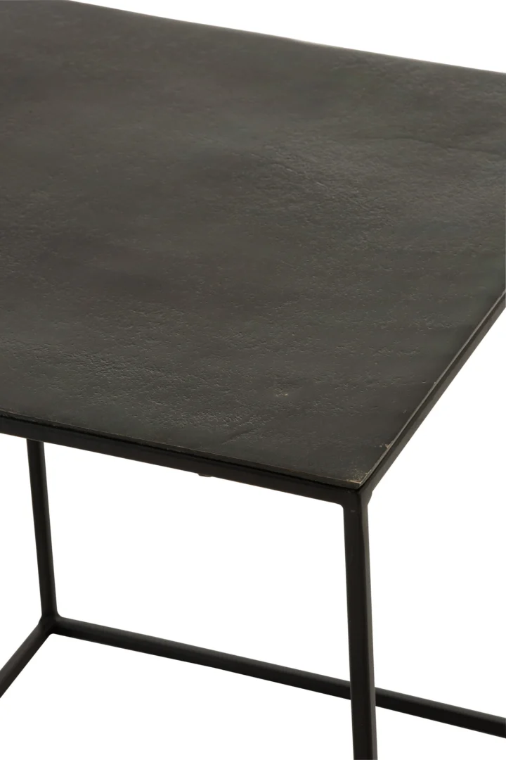 Een close-up van de hoek van de Bijzettafel Zwart Vierkant Aluminium, die het zwarte, rechthoekige aluminium frame laat zien met een dun, licht gestructureerd mat tafelblad en slanke poten.