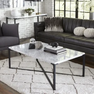 Een moderne woonkamer met een zwarte leren bank, Salontafel Zwart, Roest Organisch Marmer salontafel op een geometrisch wit vloerkleed, decoratieve objecten en boeken op tafel, grijze accentstoel en witte bakstenen muren met grote ramen.