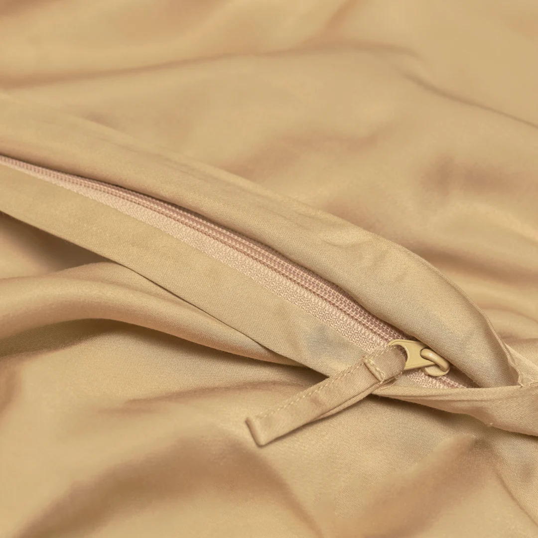 Close-up van Dekbedovertrek 200x200 Geel Luxe: beige stof met bijpassende rits gedeeltelijk open, waardoor zacht, glad materiaal en een netjes genaaide naad zichtbaar worden voor een luxe uitstraling.