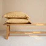 Twee okergele kussenslopen van bamboe op een houten bankje. Zachte tinten en natuurlijk licht benadrukken de zijdezachte textuur.