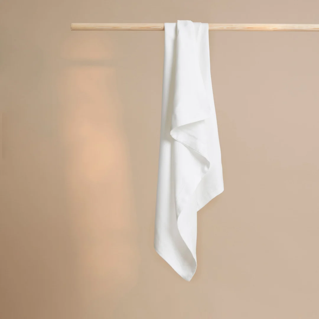 Witte bamboe kussensloop hangt aan houten stang. Zachte belichting, beige achtergrond. Hotelkwaliteit, gladde stof.