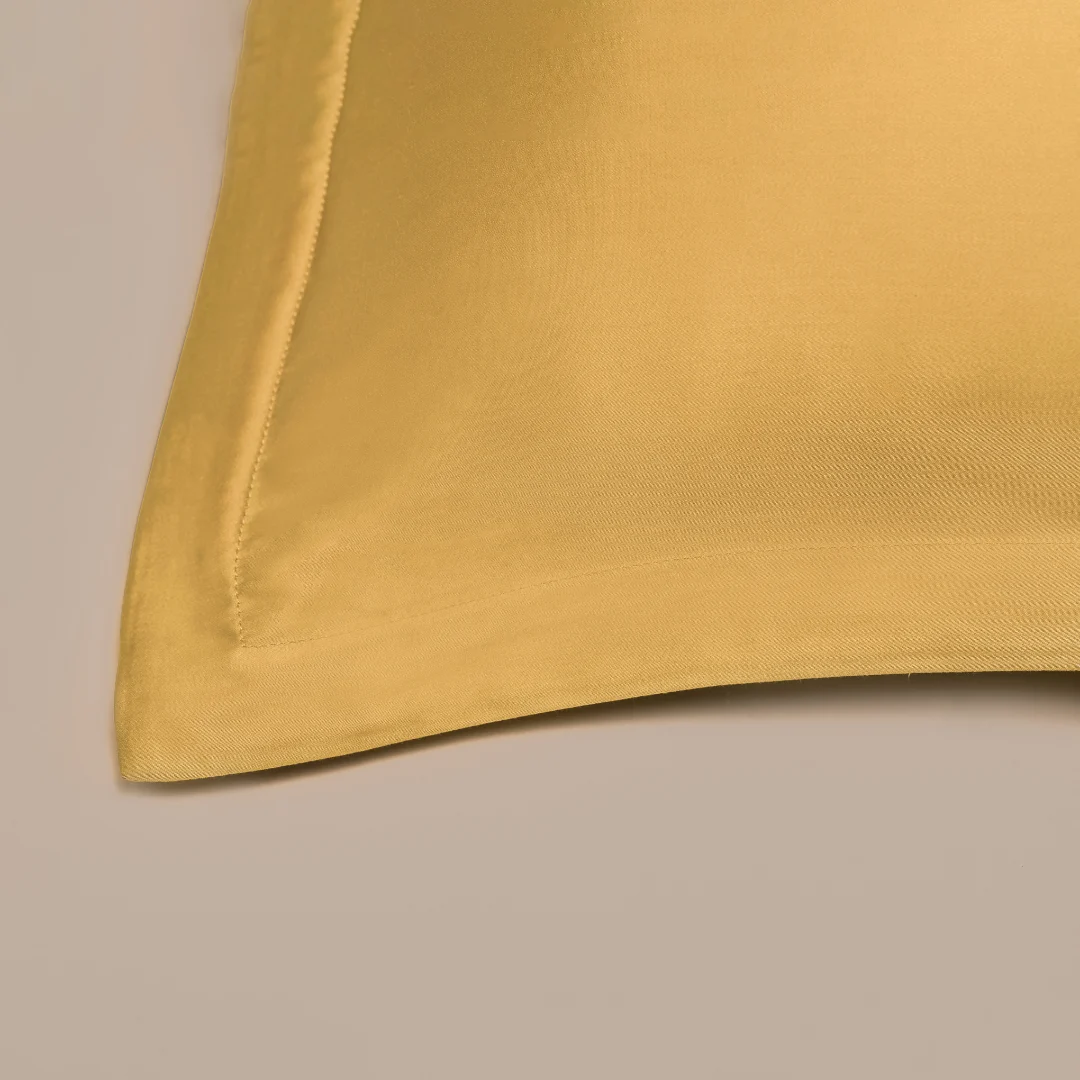 Een close-up van de Dekbedovertrek 80x80 Geel Praktisch gemak, met een goudgele satijnen afwerking met een gladde textuur en gestikte rand, weergegeven op een beige oppervlak.