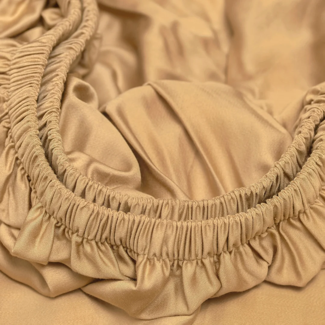 Detailopname van een okergeel hoeslaken met elastiek. Zachte stof met plooien, close-up, warme tinten en textuur. Bamboe materiaal.