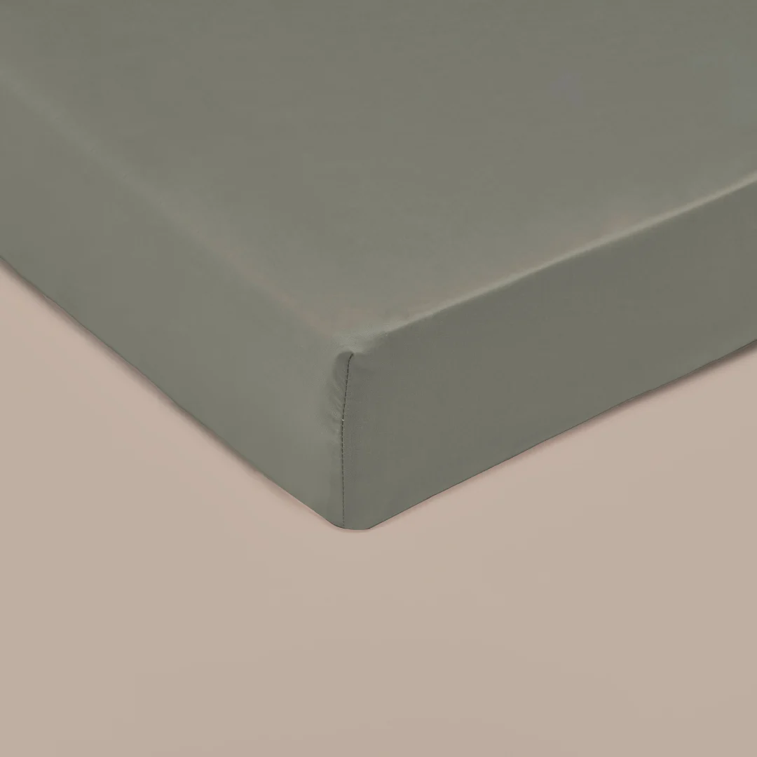 Detailopname van een olijfgroen bamboe hoeslaken op een matras. Zachte belichting, gladde textuur en strakke hoeken. Neutrale achtergrond.