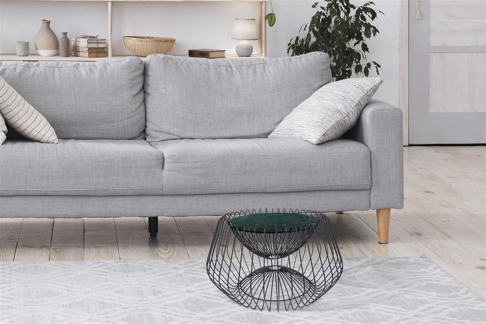 Een moderne woonkamer met een lichtgrijze bank, twee gedessineerde kussens, een Bijzettafel Zwart, Groen 37 CM Rond Marmer, een gedessineerd vloerkleed en een bladplant op de achtergrond.