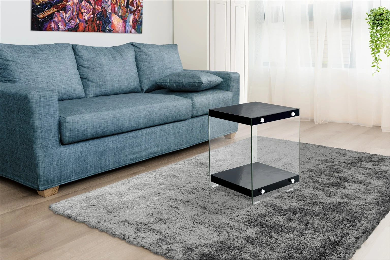 Een moderne woonkamer met een blauwe bank, een kleurrijk abstract schilderij, de Bijzettafel Zwart Glas Opbergvak op een grijs vloerkleed, een licht houten vloer, transparante witte gordijnen en een hangende groene plant.