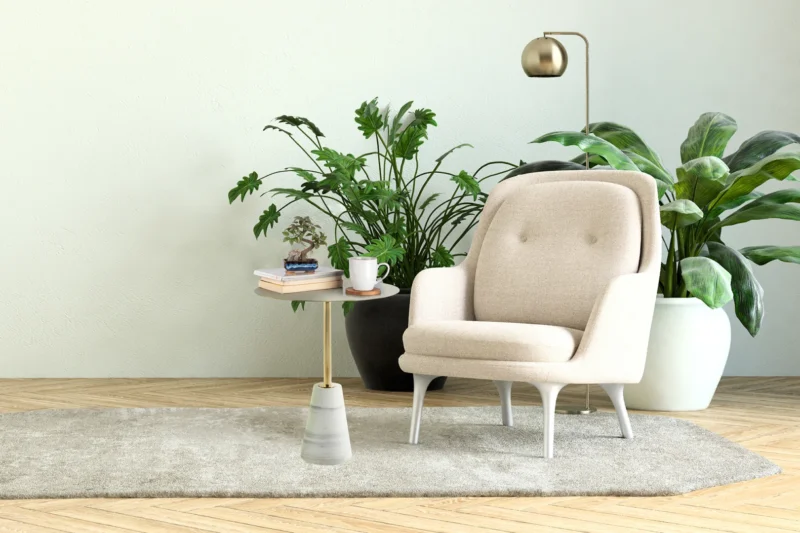 Een gezellige beige fauteuil staat naast de Bijzettafel Wit Rond Marmer Opbergvak, met daarop boeken, glazen en een mok, omringd door grote groene potplanten op een zacht vloerkleed, met een moderne vloerlamp op de achtergrond.