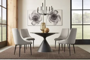 Een moderne eetkamer met de Winston stenen blad metalen onderstel ronde eettafel in zwart, gecombineerd met vier grijze stoelen, een gouden vaas en decoratieve bol bovenop, een zwarte kroonluchter bovenin en twee grote bloemenfoto's aan de muur.