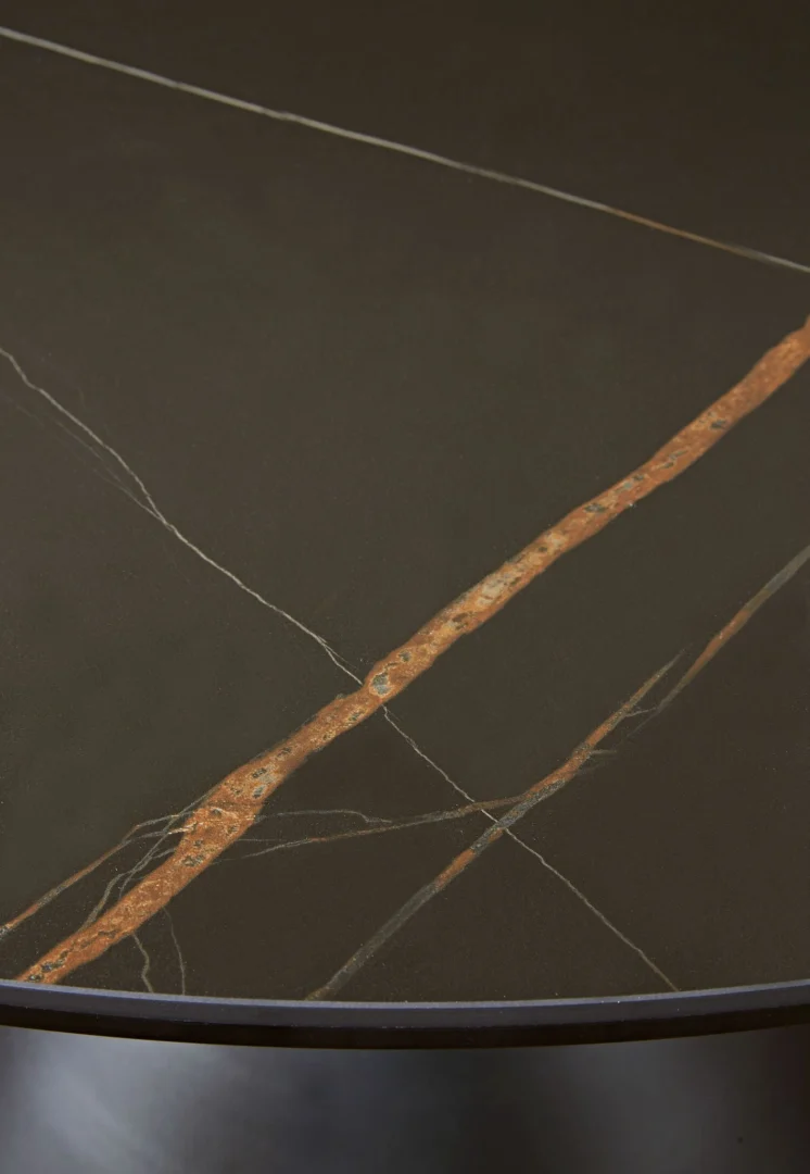 De Winston stenen blad metalen onderstel ronde eettafel in zwart heeft een rond, donker tafelblad met een opvallende roestoranje diagonale nerf en dunne witte aderen op het gladde oppervlak, wat doet denken aan natuursteen of marmer.