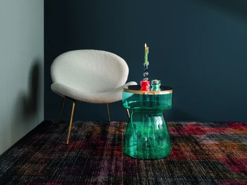 Een moderne kamer met een witte, ronde fauteuil, een blauw met gouden Bijzettafel Blauw, Goud Metaal met twee kaarsen en een veelkleurig vloerkleed tegen donkere muren.