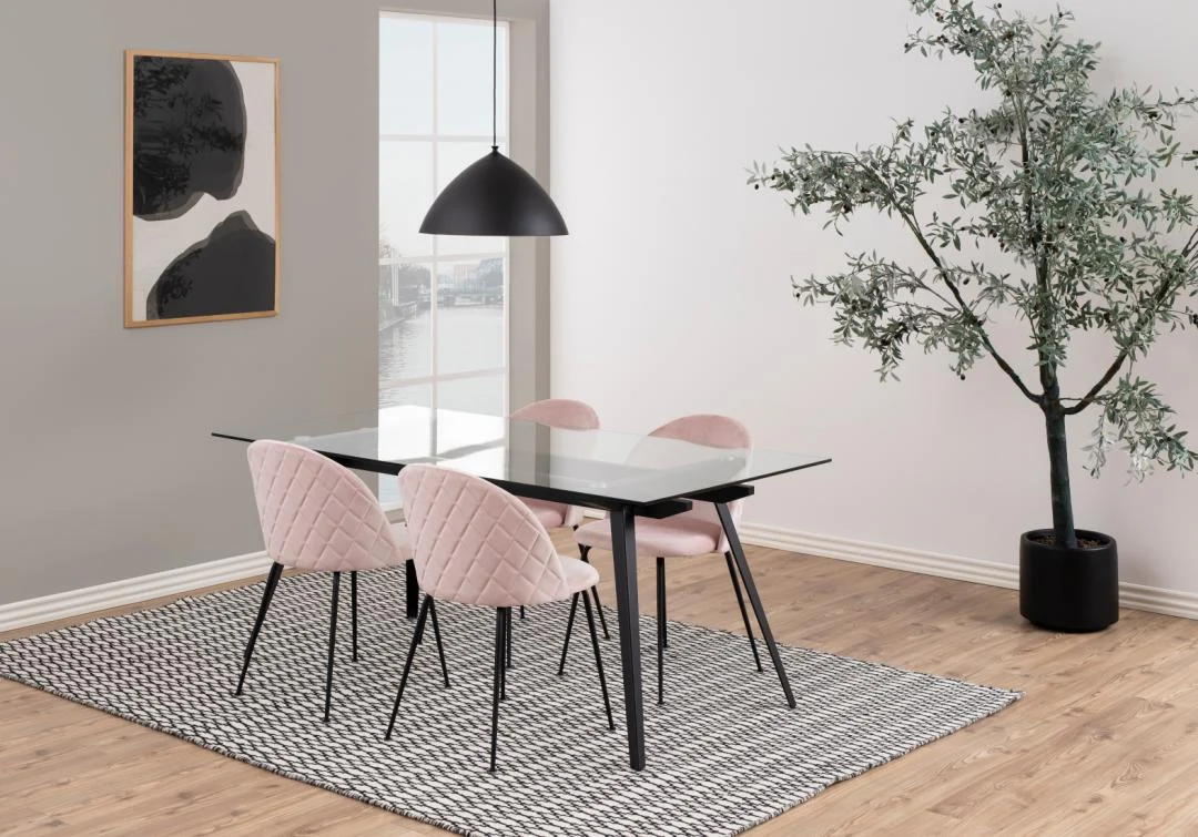 Een moderne eethoek met de Eettafel Nieuwe Sfeer glazen en stalen tafel (90 x 75 cm), vier roze gewatteerde stoelen, een zwarte hanglamp, grote abstracte muurkunst, een boom in potten en een vloerkleed met patroon op een houten vloer.