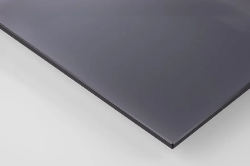 Een close-up van de Salontafel Rookglas, Zwart 40 x 45 CM laat de dunne, rechthoekige, donkergrijze rechthoekige rookglasplaat zien met gladde, glanzende oppervlakken en scherp gedefinieerde randen die rusten op een witte achtergrond.