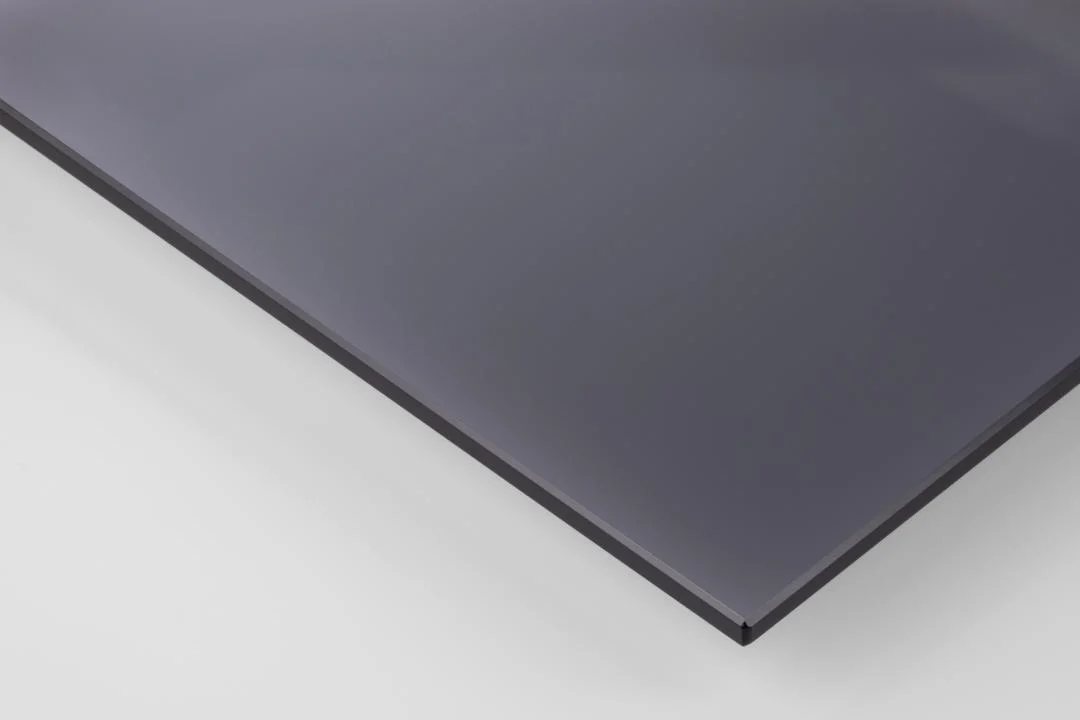 Een close-up van de Salontafel Rookglas, Zwart 40 x 45 CM laat de dunne, rechthoekige, donkergrijze rechthoekige rookglasplaat zien met gladde, glanzende oppervlakken en scherp gedefinieerde randen die rusten op een witte achtergrond.