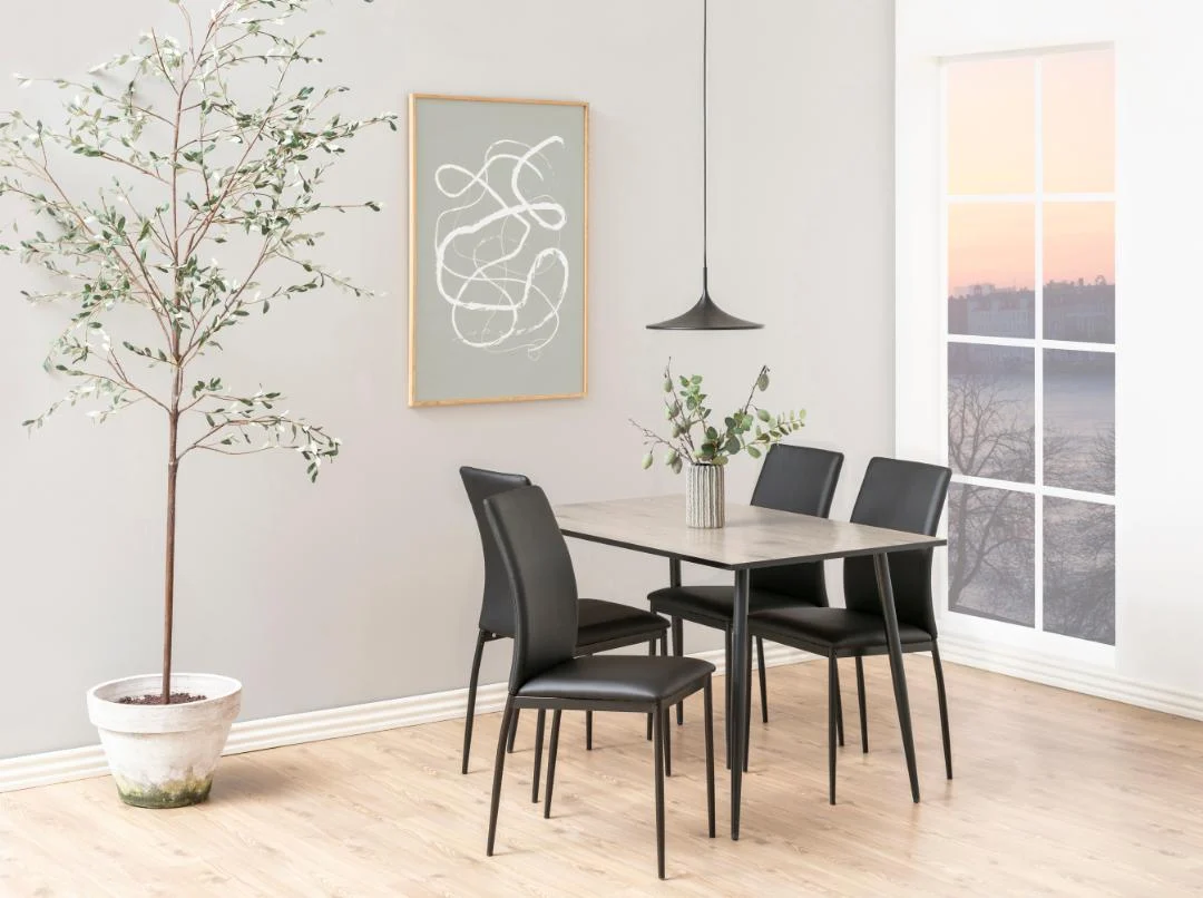 Minimalistische eethoek met de Eettafel Wilma 80 x 75 CM Rond Eikenhout tafel met een mat zwart onderstel, vier zwarte stoelen, boom in pot, abstracte kunst, hanglamp en groot raam met uitzicht op een zonsondergang. Licht houten vloer en neutrale muren.