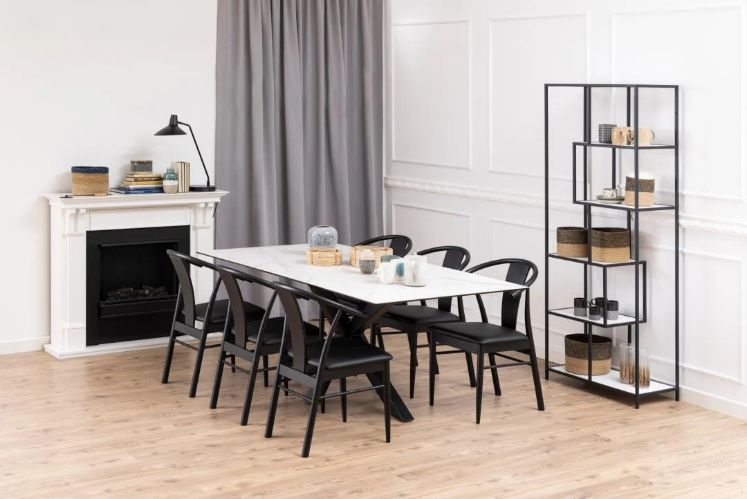 Een moderne eetkamer met de Eettafel Nieuwe Sfeer 200 x 100 CM (rechthoekig keramiek en staal), zes zwarte stoelen, een zwarte metalen plank met decor, een witte open haard, bureaulamp, rieten manden, grijze gordijnen en een lichthouten vloer.