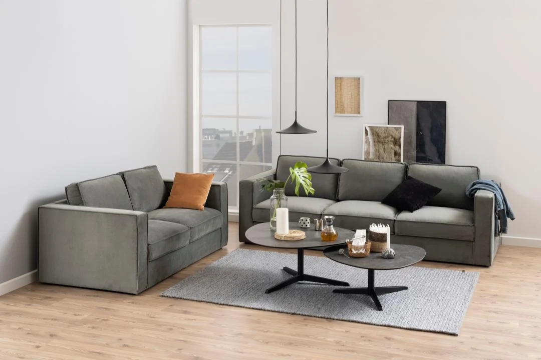 Een moderne woonkamer met twee grijze banken, een grijs vloerkleed en de Salontafel Zwart 95 x 41 CM Driehoek (kunststof) als salontafel met drankjes en decor. Neutrale muurkunst, een lichte houten vloer en een groot raam fleuren de ruimte op.