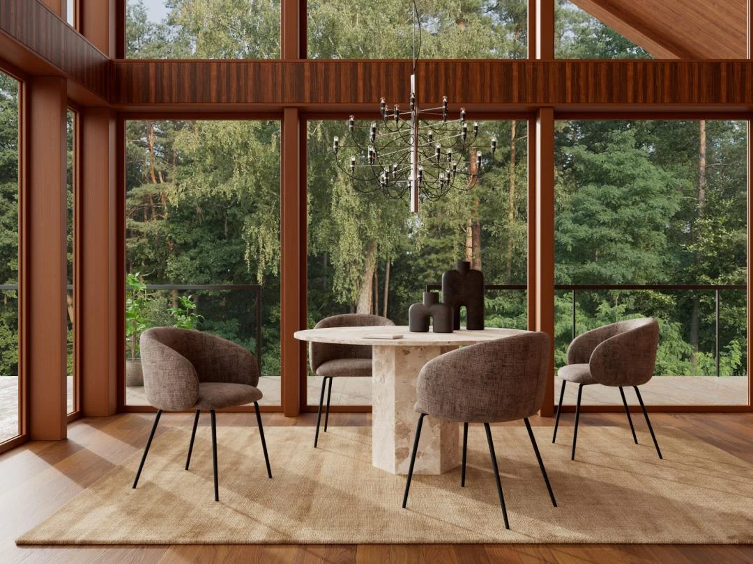 Een moderne eetkamer met grote ramen, een beige vloerkleed, vier gestoffeerde stoelen, een zwarte kroonluchter en de Eettafel Naxos 130 CM Rond Marmer Massief tafel, met uitzicht op een weelderig groen bos.