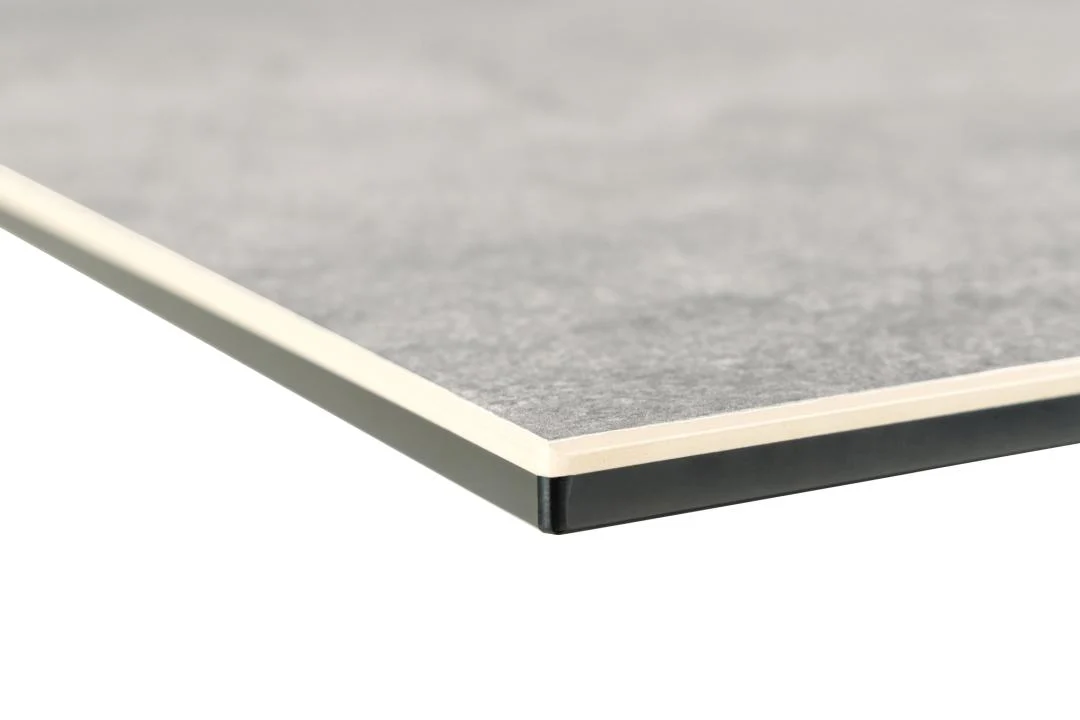 Close-up van de hoek van de Eettafel Nieuwe Sfeer 200 x 100 CM, een rechthoekige tafel met gelaagde grijze keramiek en stalen randen, met een dunne beige middenlaag en een zwart onderstel tegen een effen achtergrond.