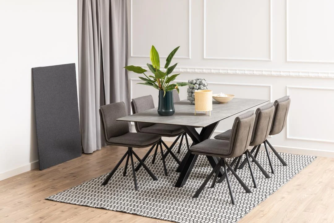 Een moderne eetkamer met de Eettafel Nieuwe Sfeer 200 x 100 CM rechthoek keramiek staal, zes grijze stoelen, een gedessineerd vloerkleed, een vaas met groene bladeren, grijze gordijnen, een luifel en een houten vloer.