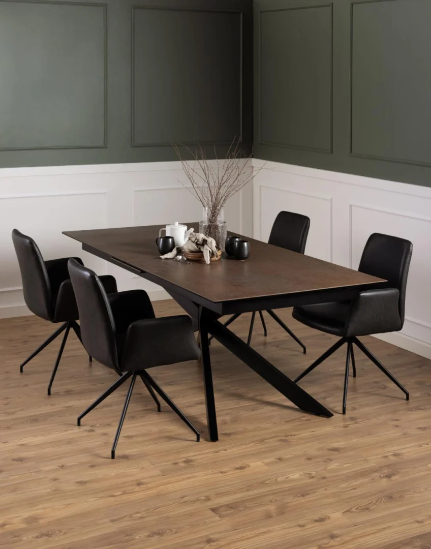 Een moderne eetkamer met de Eettafel Nieuwe Sfeer 240 x 100 CM, een rechthoekige tafel van glas en staal, vier zwarte draaistoelen, minimalistische kaarsen en vazen, lichthouten vloeren en groen-witte wanden.