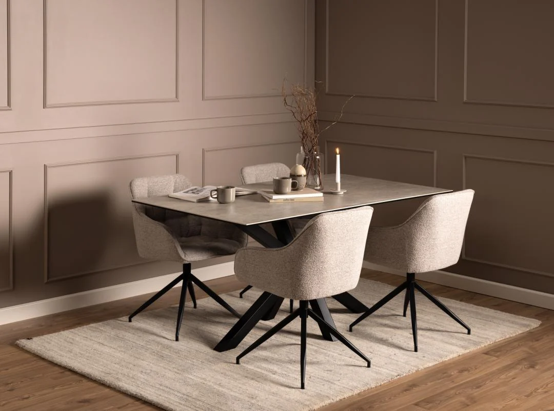 Een eigentijdse eethoek met de Eettafel Nieuwe Sfeer 160 x 90 CM, vier beige gestoffeerde stoelen, een beige vloerkleed en minimalistische decoraties - kaarsen, vazen en gedroogde takken - tegen een taupekleurige wand met panelen.