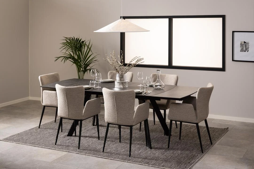 Een moderne eetkamer met de Eettafel Nieuwe Sfeer 97 x 75 CM rechthoek glas tafel, zes beige gestoffeerde stoelen, servies, een vaas met takken, een hanglamp, potplant, muurkunst op grijze muren en een grijs vloerkleed eronder.