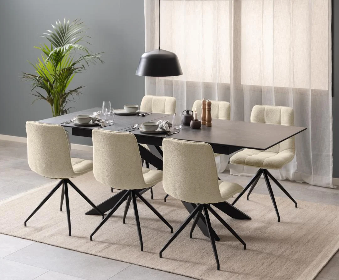 Moderne eetkamer met de Eettafel Irwine 90 x 76 CM Rechthoek in zwart keramiek en staal, zes crèmekleurige stoelen met zwarte poten, een tafel voor zes personen, een zwarte hanglamp, een plant in potten en transparante gordijnen voor de grote ramen.
